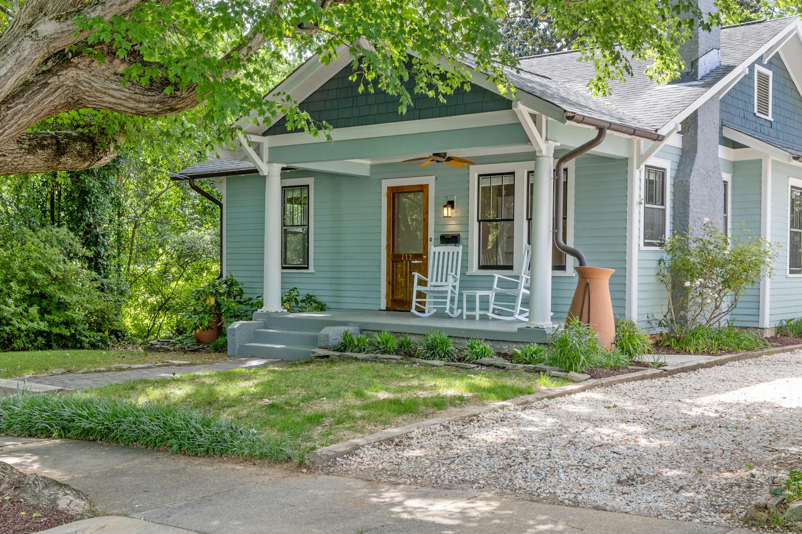 Quaint suburban home with a cozy porch and rocking chairs, surrounded by lush greenery.