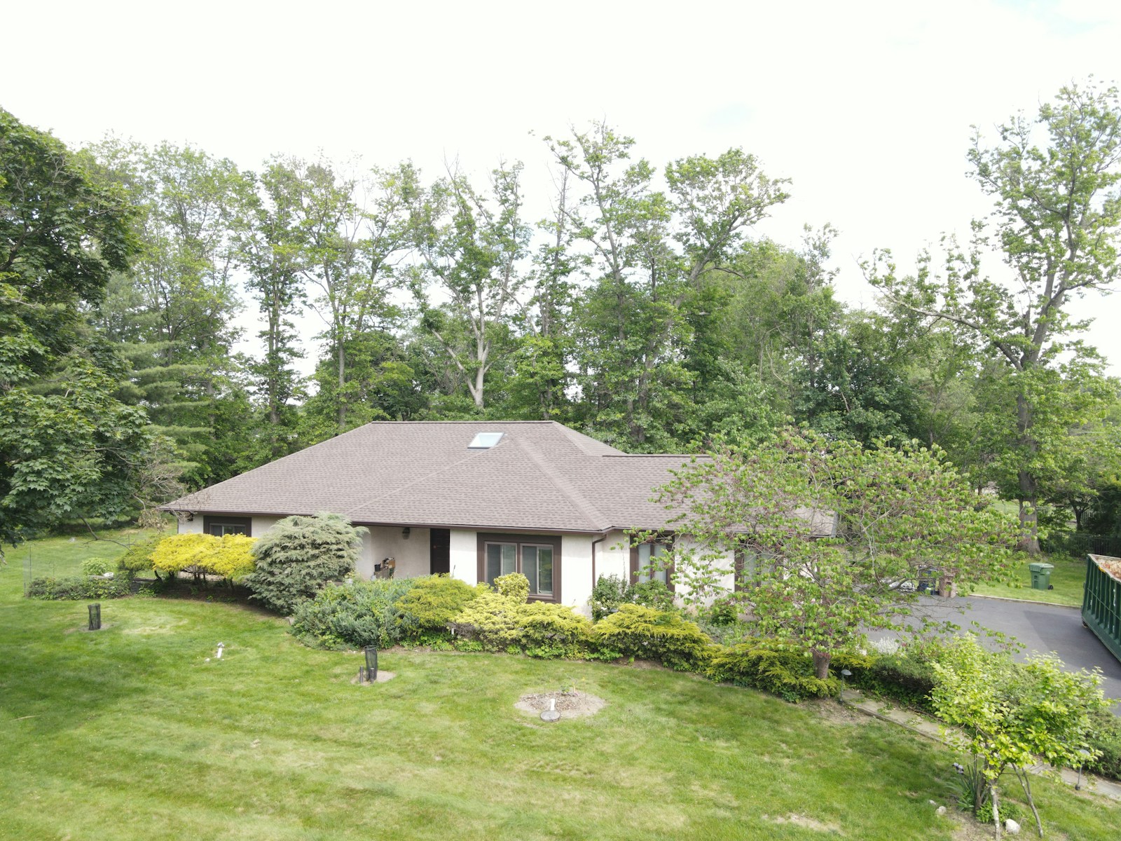 A suburban house nestled among trees on a grassy hill.